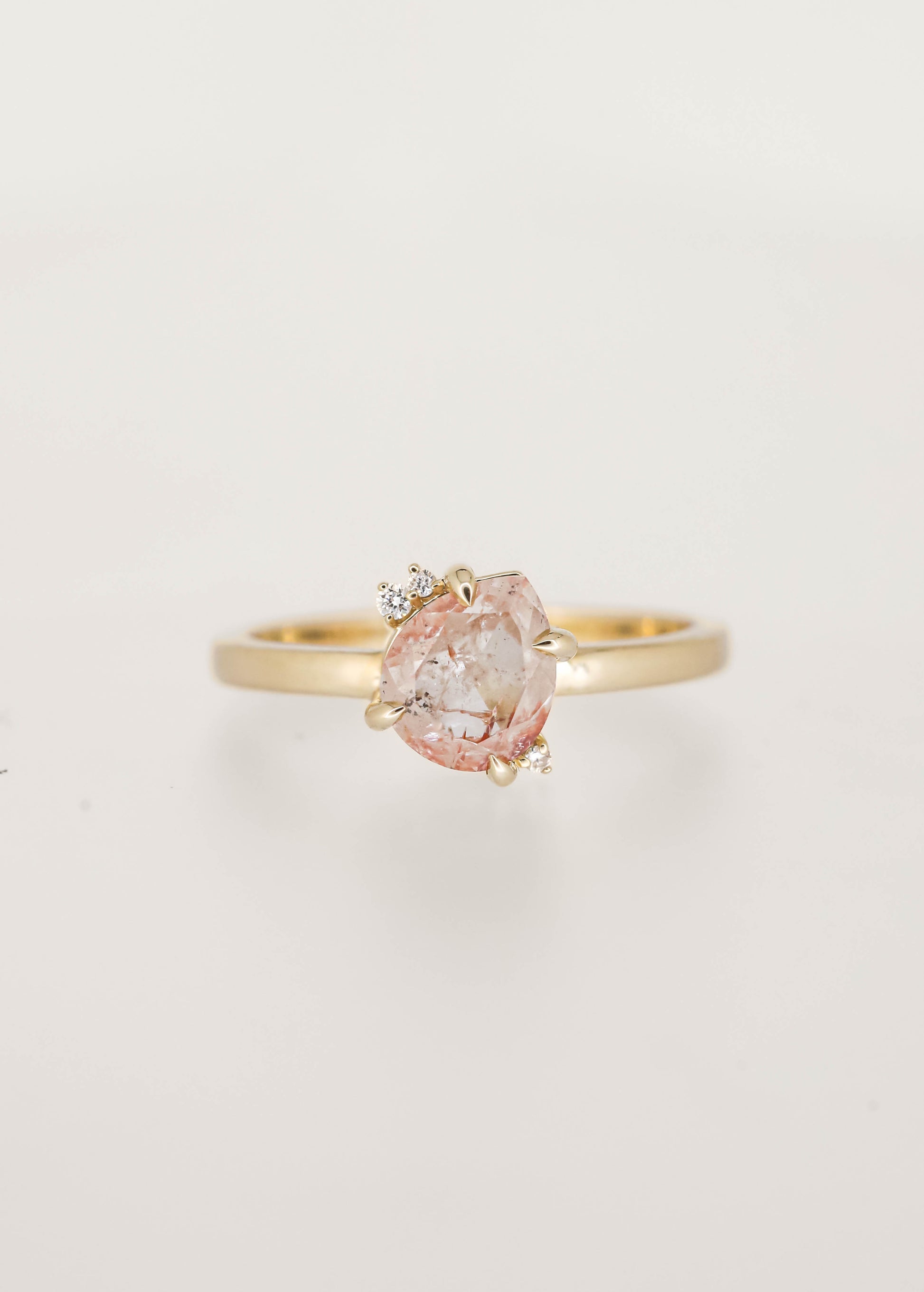 Dainty squatty pear salt and pepper diamond engagement ring in 14K yellow gold with a tilted four prong setting and two round diamond accents