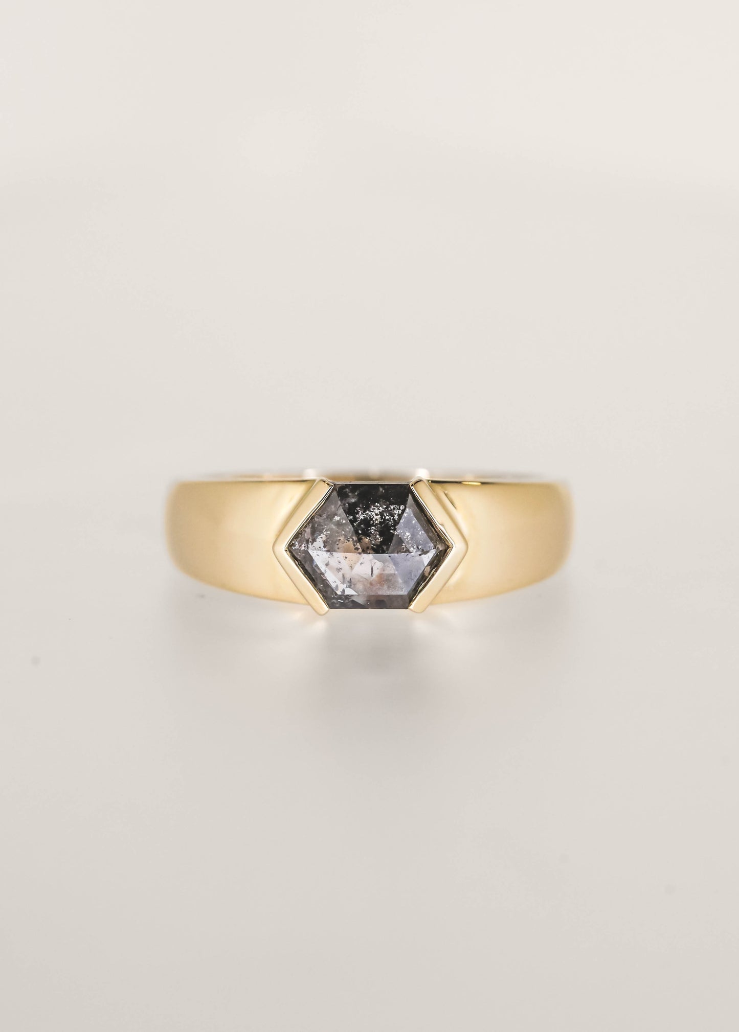 Gender neutral masculine east west hexagon salt and pepper diamond engagement ring in 14K yellow gold with a wide domed band and half bezels