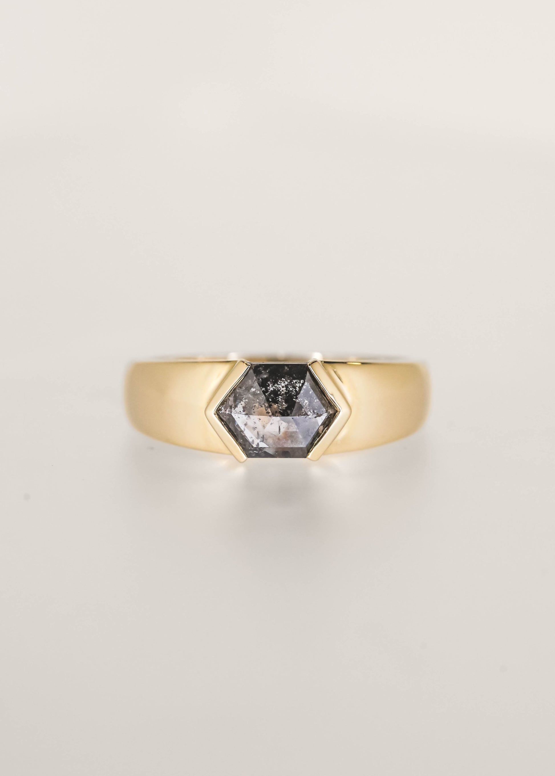 Gender neutral masculine east west hexagon salt and pepper diamond engagement ring in 14K yellow gold with a wide domed band and half bezels