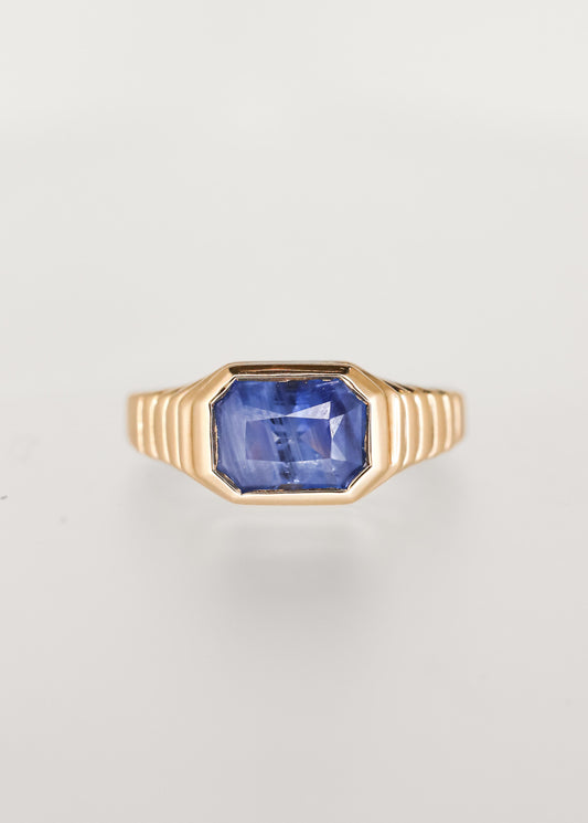 Masculine leaning east west emerald cut blue sapphire engagement ring in 14K yellow gold with a sculptural ribbed signet bezel