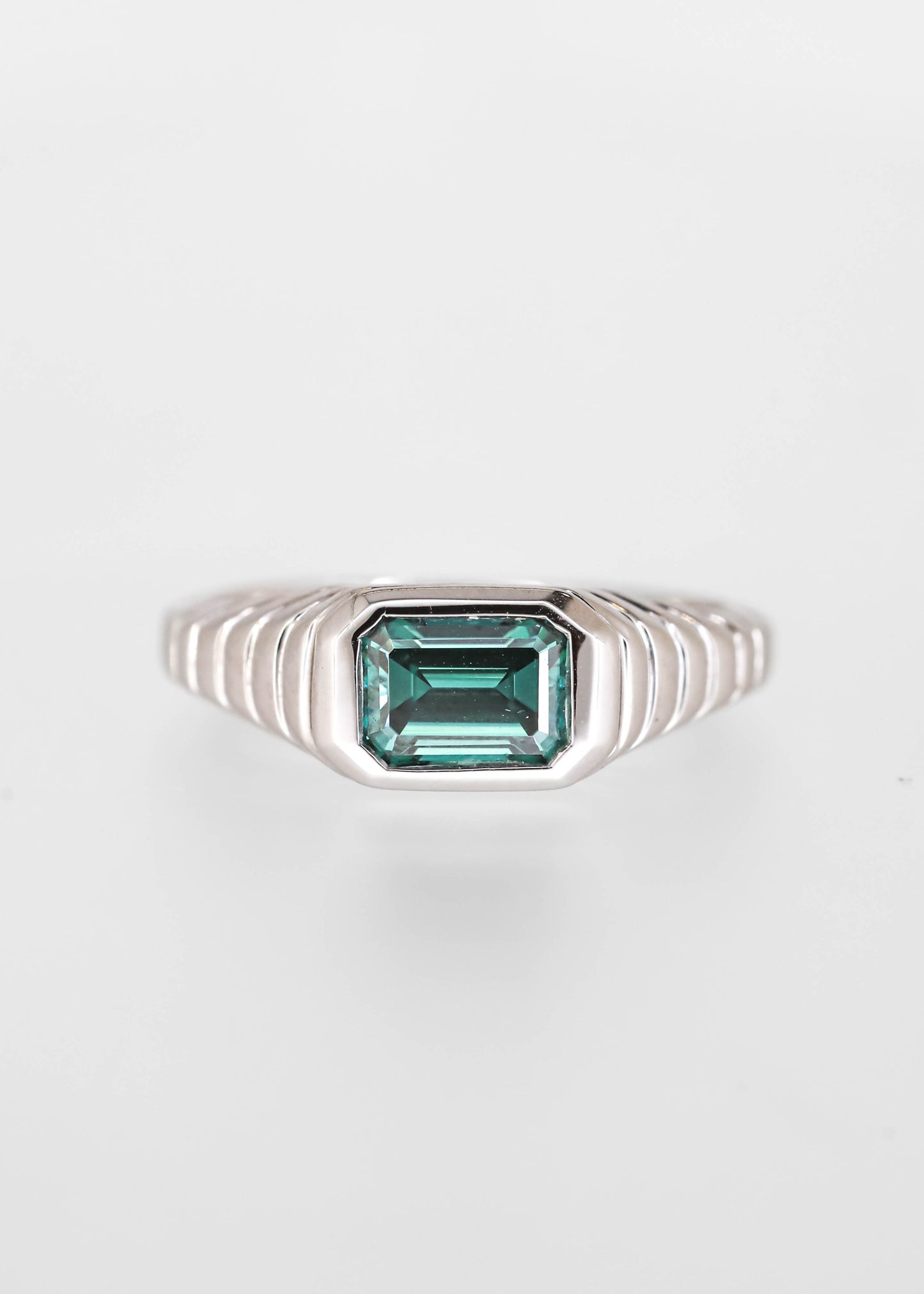 Gender neutral east west emerald cut teal moissanite engagement ring in 14K white gold with a sculptural ribbed signet bezel