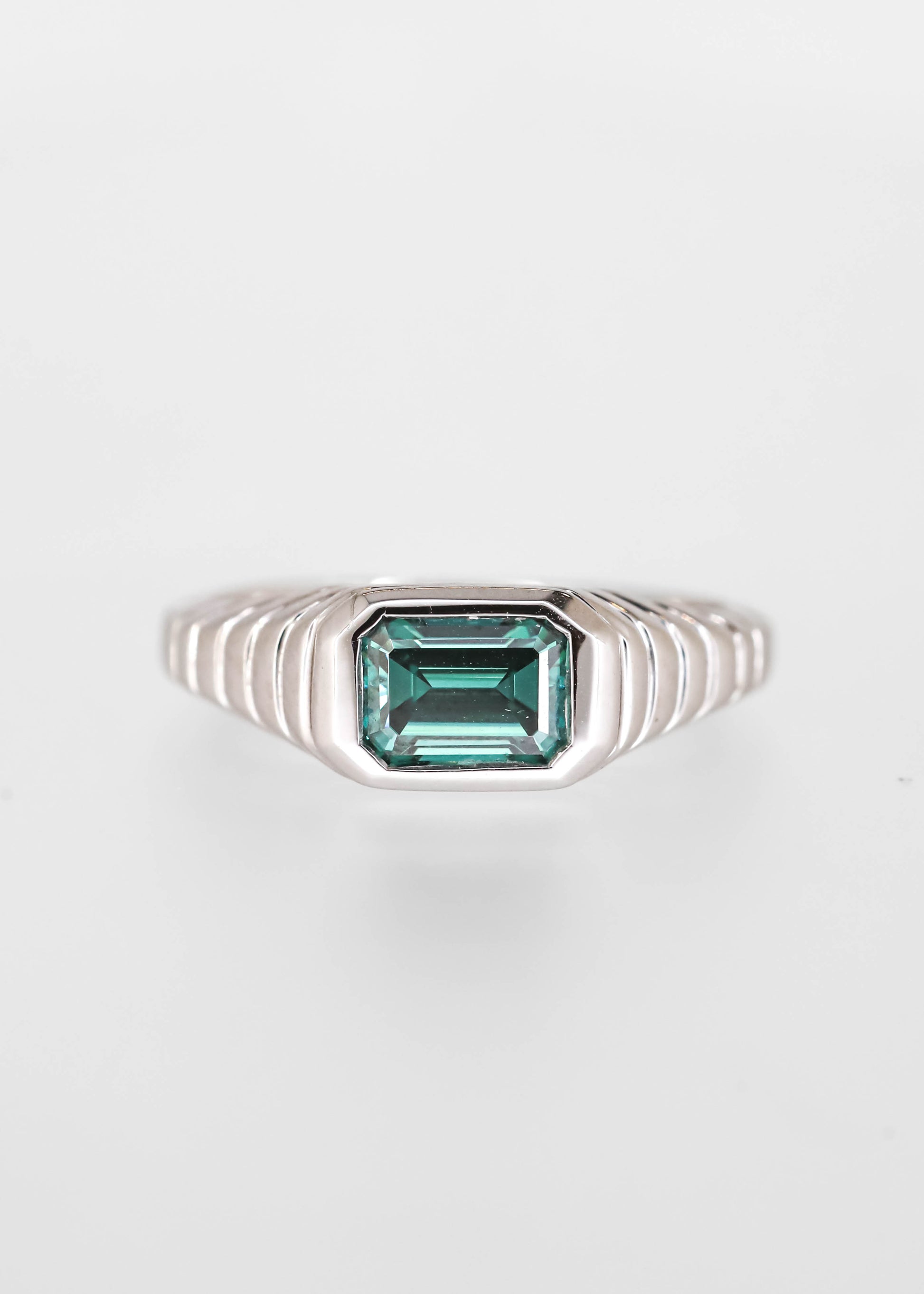 Gender neutral east west emerald cut teal moissanite engagement ring in 14K white gold with a sculptural ribbed signet bezel