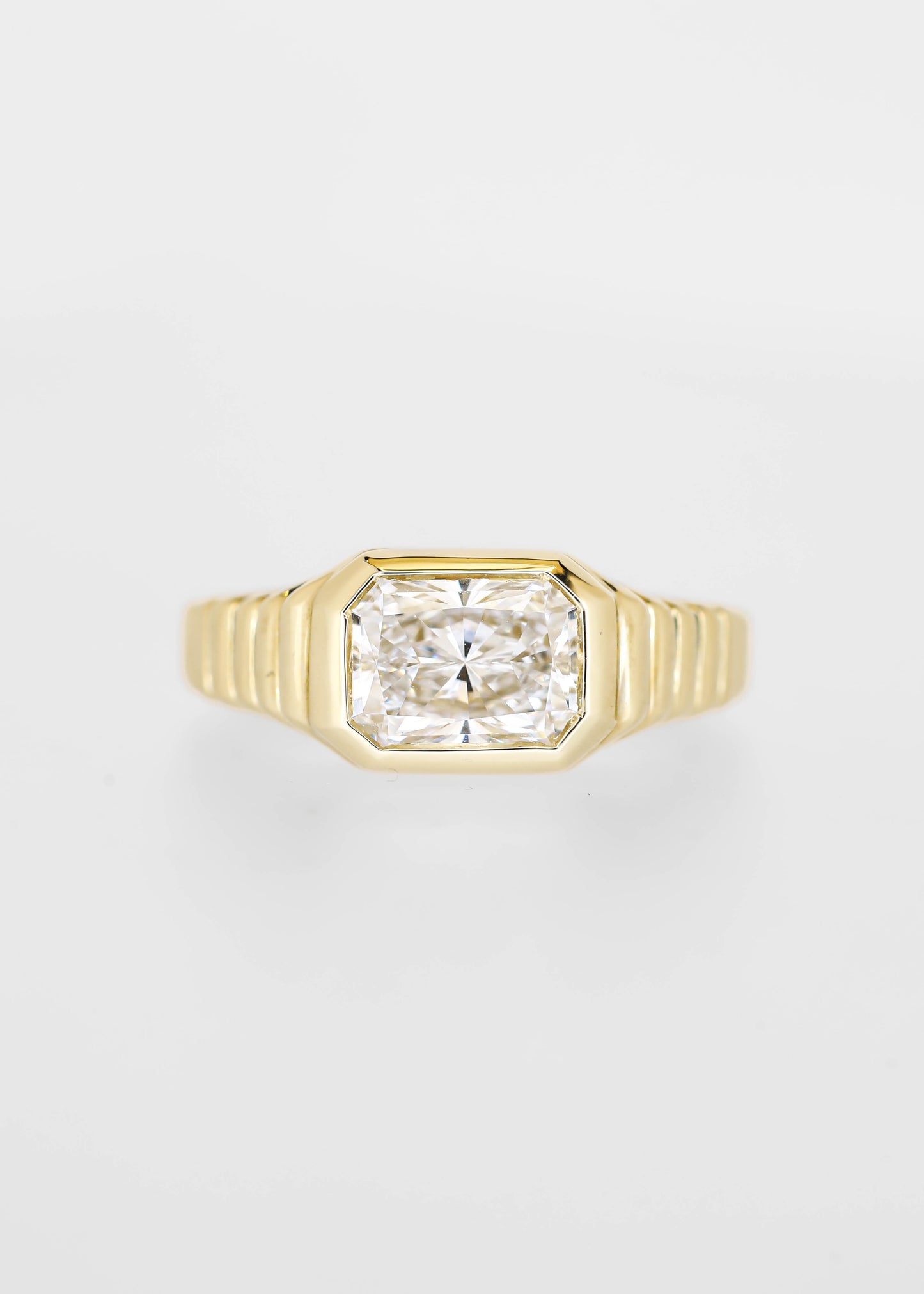 East west bezel set radiant cut lab grown diamond engagement ring in 14K yellow gold with a ribbed band