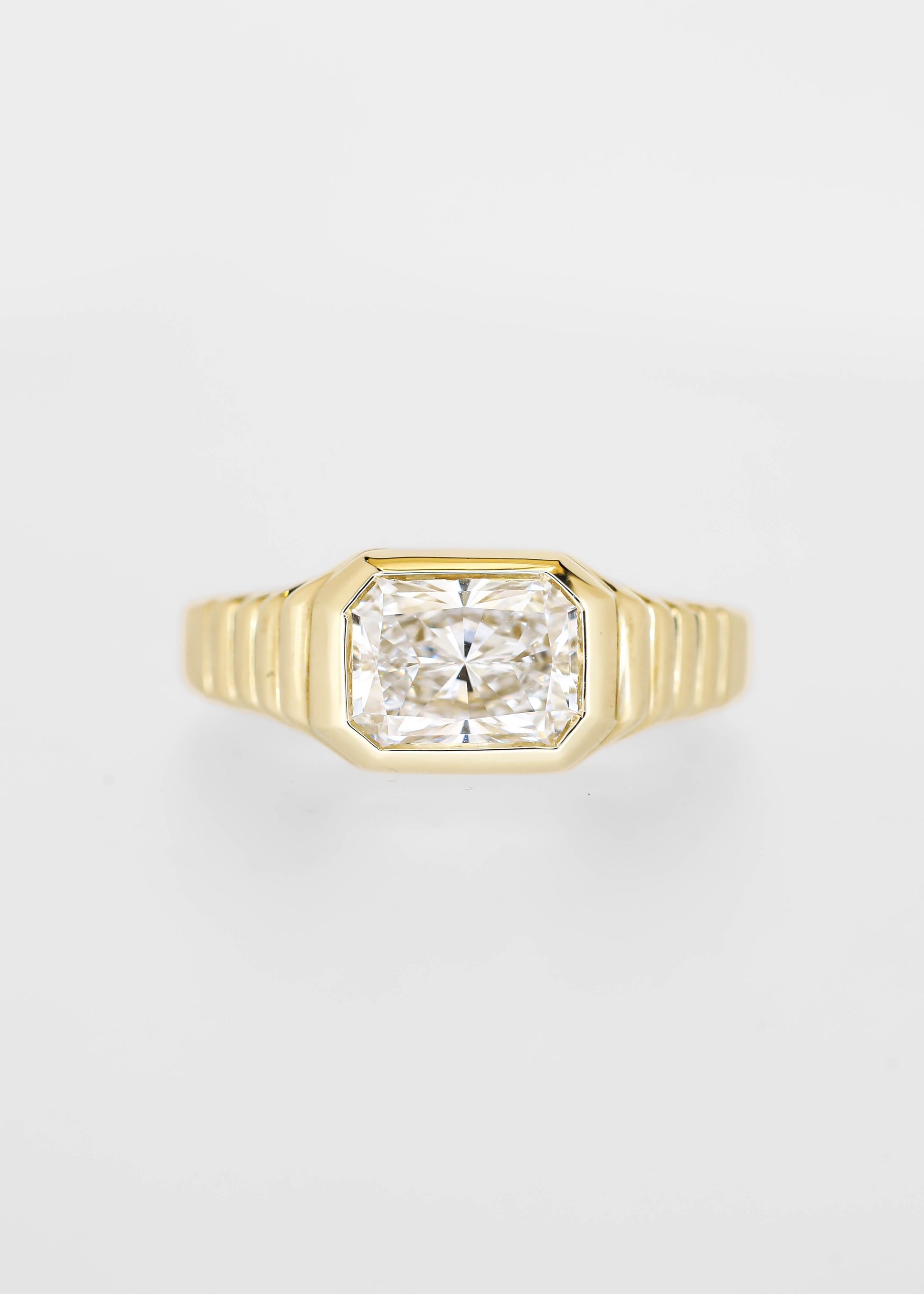 East west bezel set radiant cut lab grown diamond engagement ring in 14K yellow gold with a ribbed band