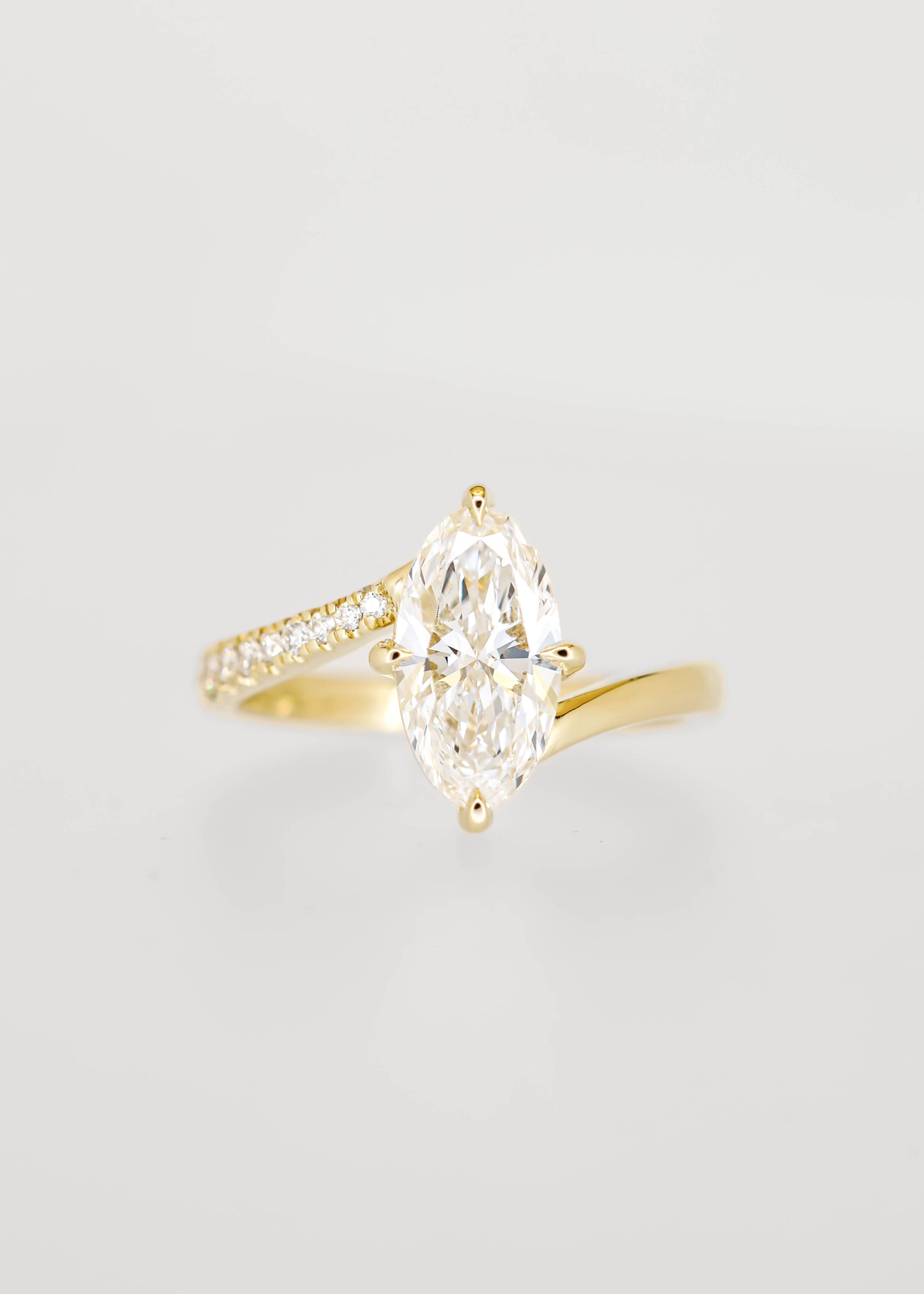 Moval cut lab grown diamond engagement ring in 14K yellow gold with an asymmetric bypass band and pavé accents