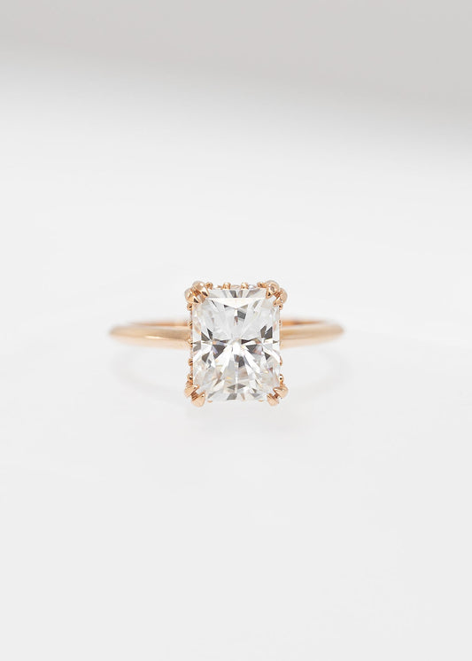 Radiant cut moissanite solitaire engagement ring in 14K rose gold with a double claw basket and hidden halo