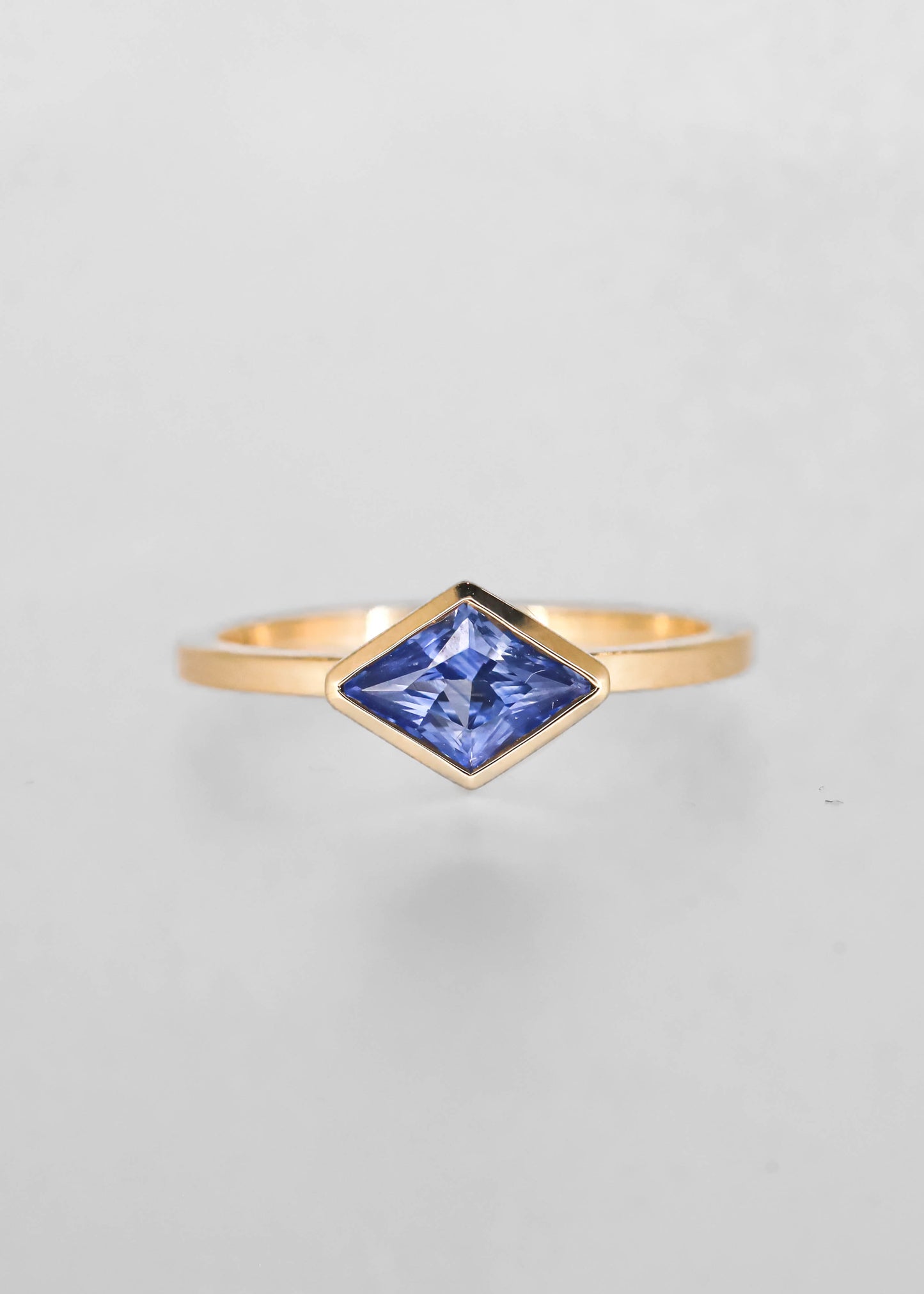 Minimal east west lozenge cut blue sapphire engagement ring in 14K yellow gold with a full bezel and slim band