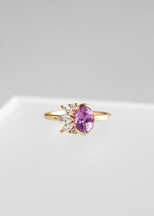 Oval pink sapphire engagement ring in 14K yellow gold with a half bezel and asymmetrical marquise and round diamond cluster