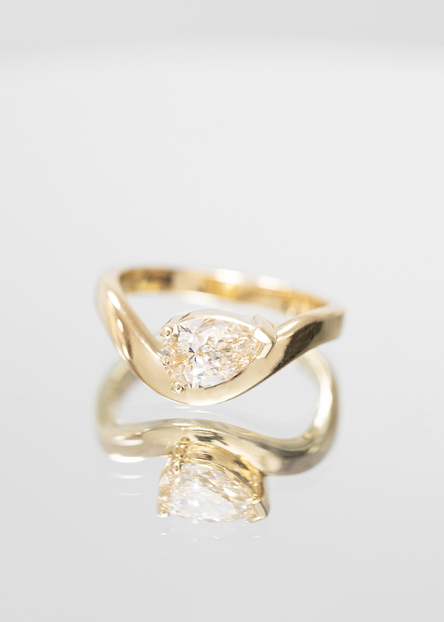 Elegant gender-neutral solitaire engagement ring featuring a 1ct pear-shaped diamond, set in a unique thick curved band design of polished yellow gold. This ring is part of our exclusive collection, perfect for those seeking a modern yet timeless piece. The design showcases a bold, minimalist aesthetic with a focus on the stunning clarity and brilliance of the diamond, making it an ideal choice for anyone looking for a distinctive, bold engagement ring.