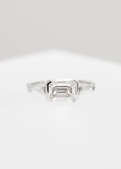 East west emerald cut moissanite three stone engagement ring in 14K white gold with half bezels and tapered baguette side stones